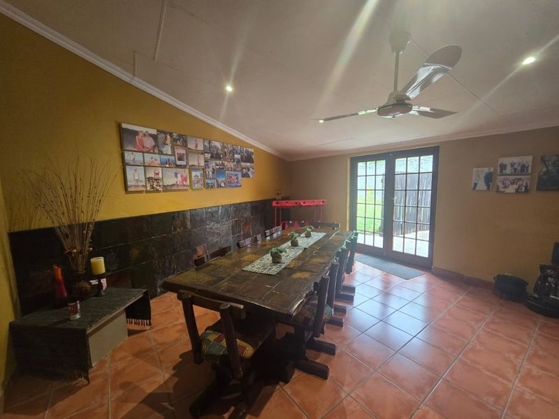 Dining room featuring terracotta floor tiles, slate wall accents, ceiling fan, and double glass doors providing access to the outdoor area.