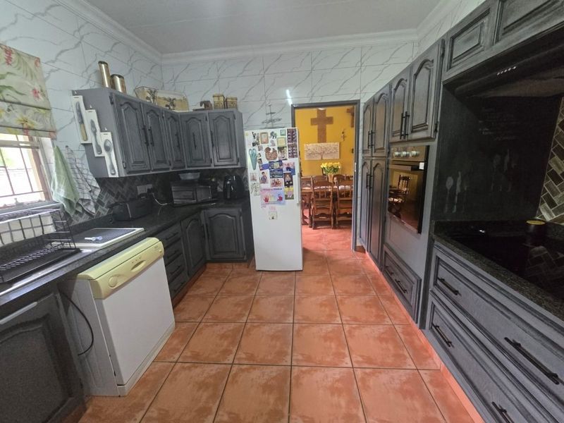 A functional kitchen featuring dark grey cabinetry, granite countertops, built-in oven, and tiled flooring, with a direct view into the adjacent dining area.