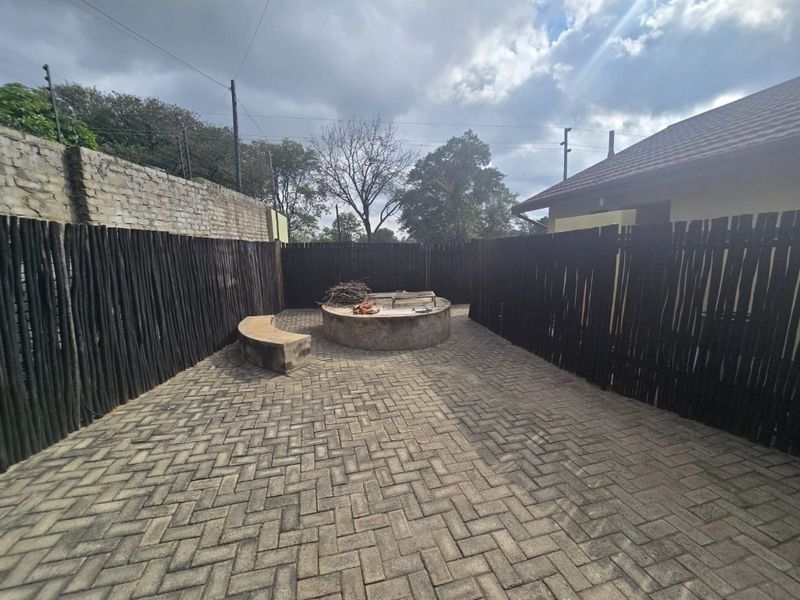Outdoor patio area featuring a paved floor, built-in circular fire pit with a concrete bench, and enclosed by timber pole fencing.