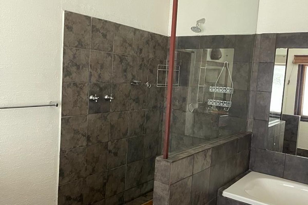 A bathroom featuring a walk-in shower with a glass screen, built-in bathtub, and dark tiled finishes throughout.