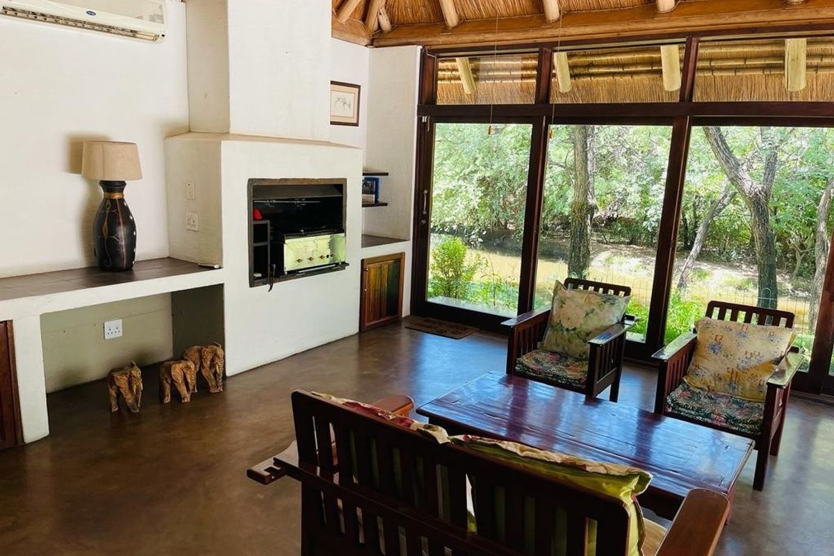 Spacious living area featuring a traditional thatched roof, built-in fireplace, polished concrete floors, and large glass doors opening to a scenic outdoor view.