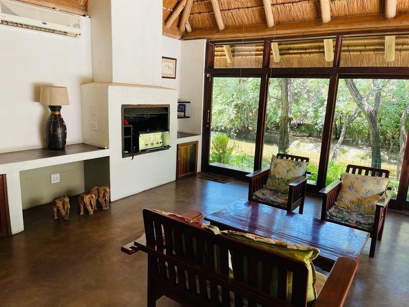 Spacious living area featuring a traditional thatched roof, built-in fireplace, polished concrete floors, and large glass doors opening to a scenic outdoor view.