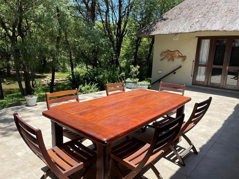 A spacious outdoor patio featuring tiled flooring and a thatched roof, providing a comfortable area for relaxation overlooking the surrounding natural landscape.
