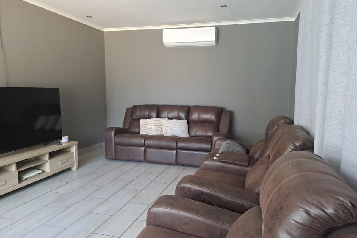 A well-maintained living room featuring neutral grey walls, tiled flooring, recessed downlighting, and a wall-mounted air conditioning unit.