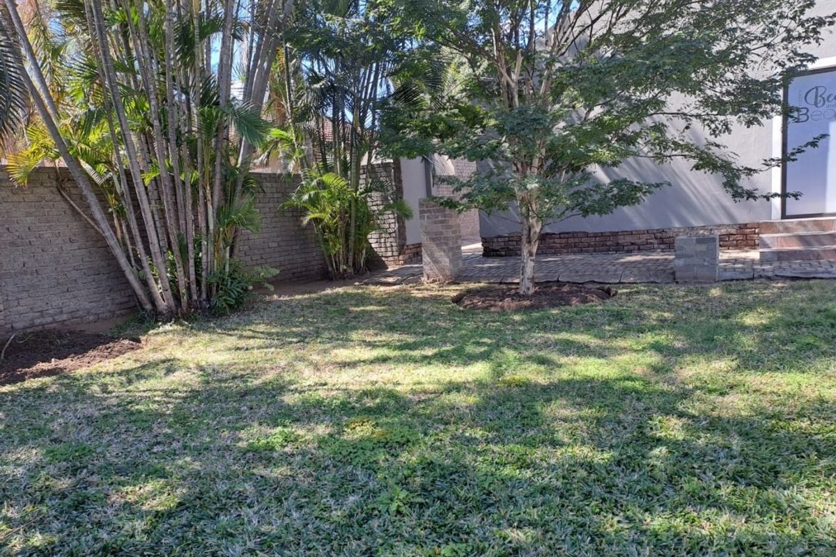 A private rear garden featuring a lawn, established trees, and a paved patio area adjacent to the main building structure.