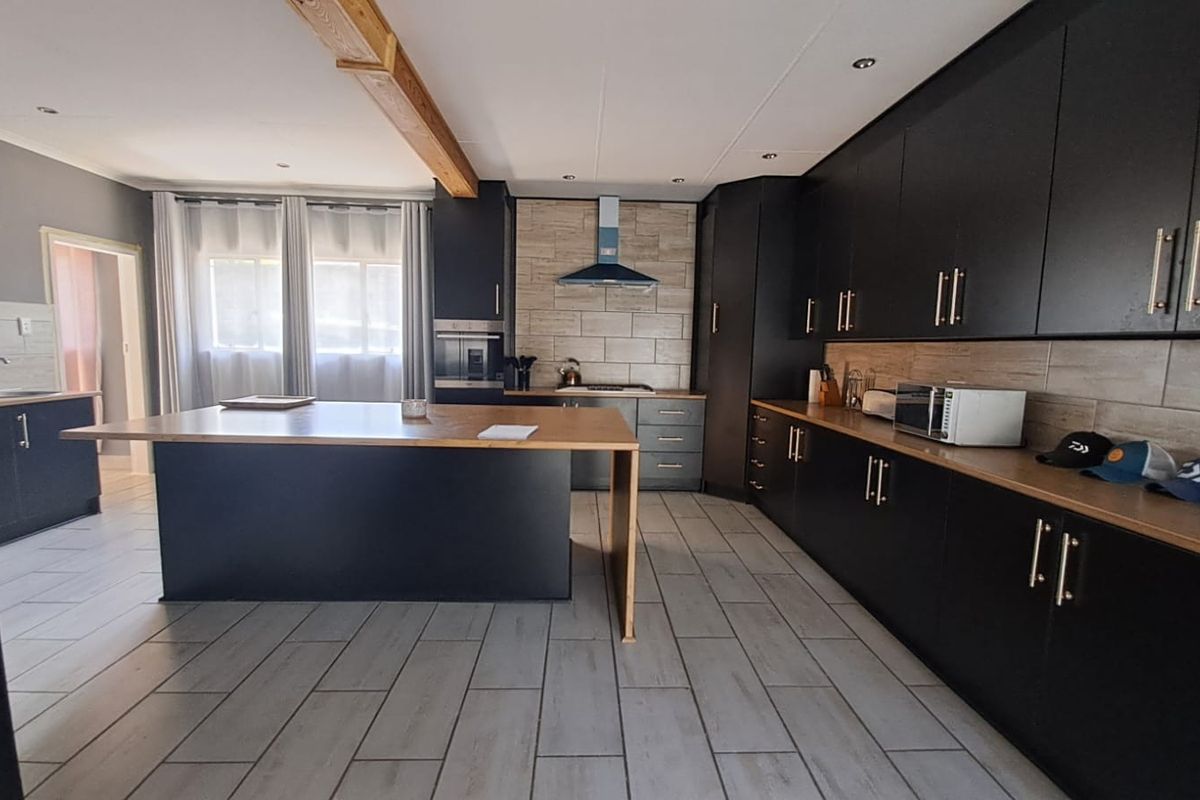 Modern kitchen featuring dark cabinetry, a large central island, tiled flooring, and an exposed timber beam, offering a contemporary and functional cooking space.