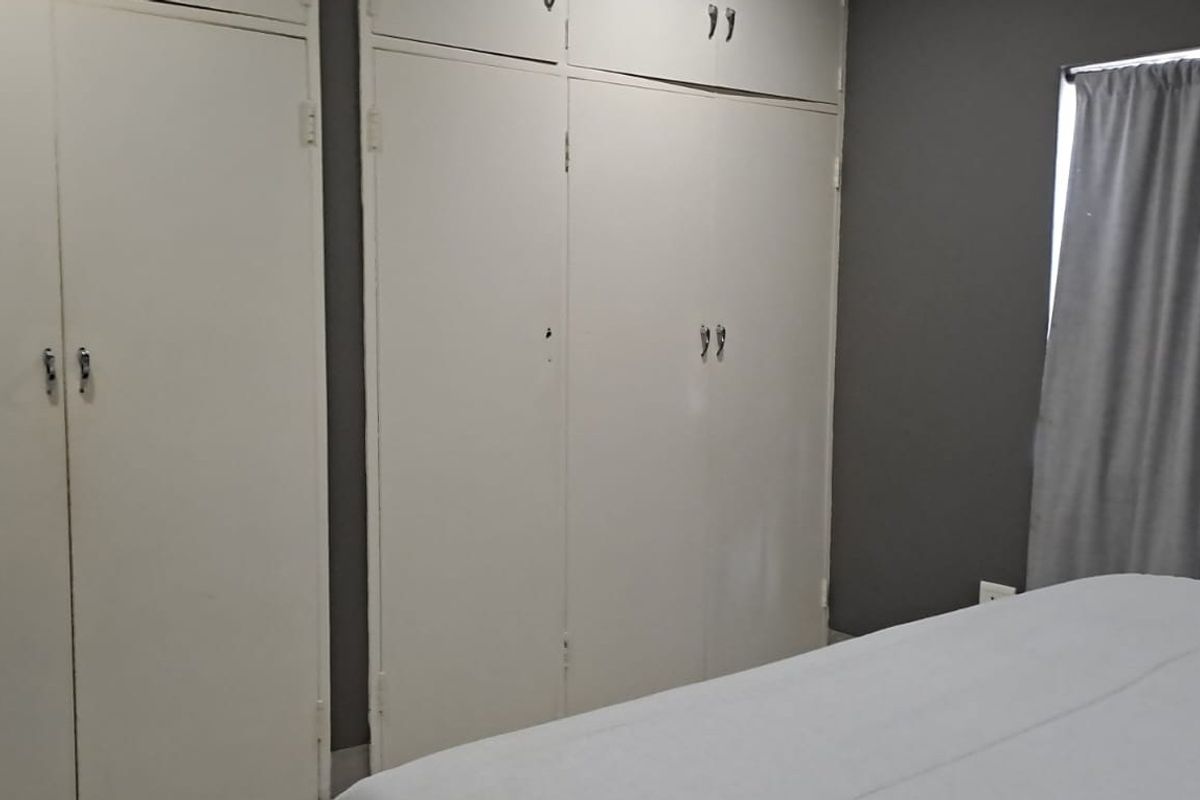 A bedroom featuring built-in cupboards with a neutral grey wall finish and window treatments.
