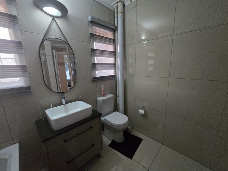 A modern bathroom featuring a vessel sink on a vanity cabinet, tiled walls, and a toilet, with an exposed plumbing pipe visible.