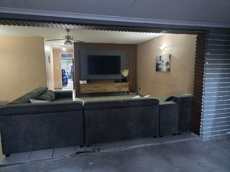 Living room featuring a slatted wood feature wall, wall-mounted media unit, ceiling fan, and tiled flooring.
