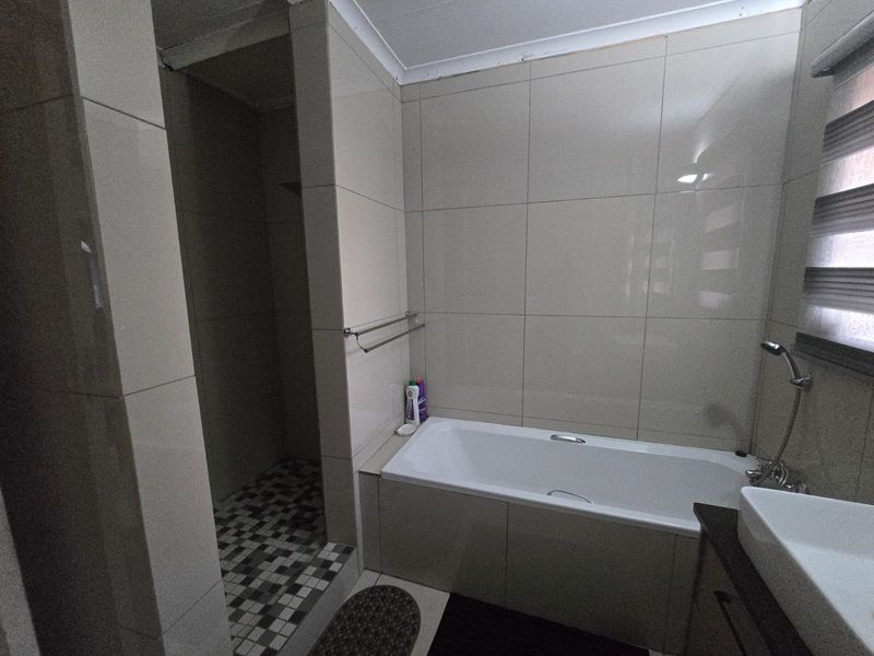 A functional bathroom featuring a built-in bathtub, separate walk-in shower, and tiled finishes throughout.