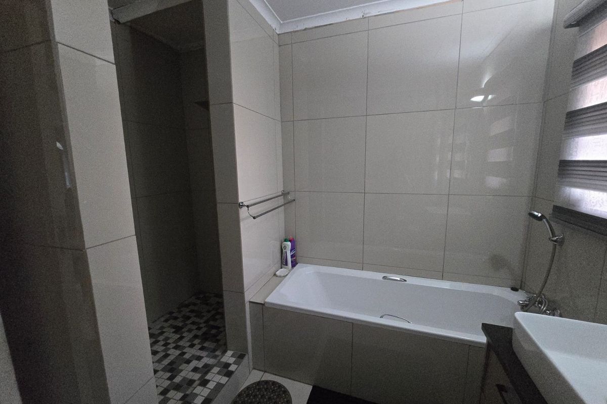 A functional bathroom featuring a built-in bathtub, separate walk-in shower, and tiled finishes throughout.