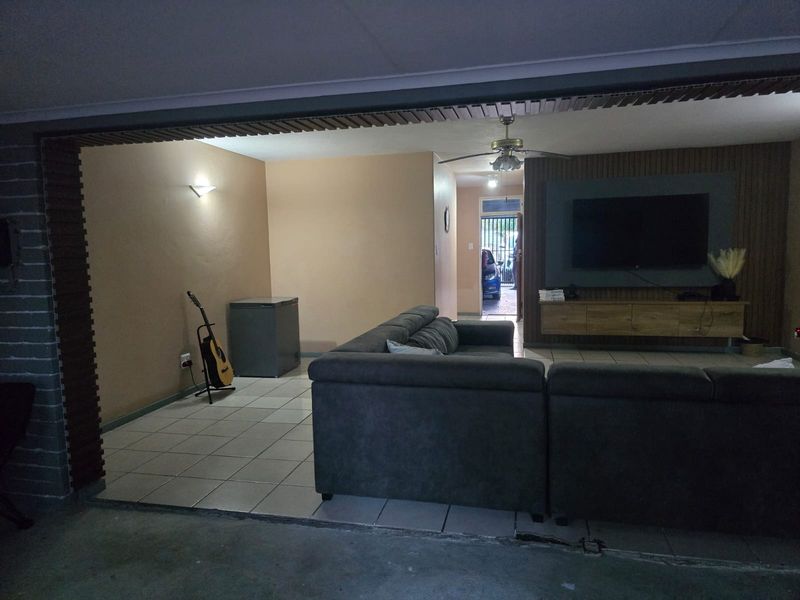 A living room featuring tiled flooring, a ceiling fan, and decorative wall paneling with a built-in media unit.