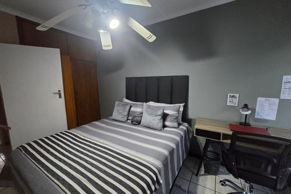 A functional bedroom featuring tiled flooring, built-in wooden cupboards, and a ceiling fan, providing a practical living space.