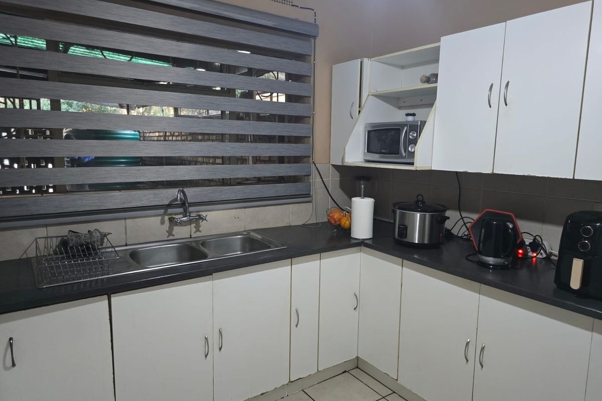 A functional kitchen featuring white cabinetry, dark laminate countertops, a double basin sink, and tiled flooring, providing a practical workspace for daily use.