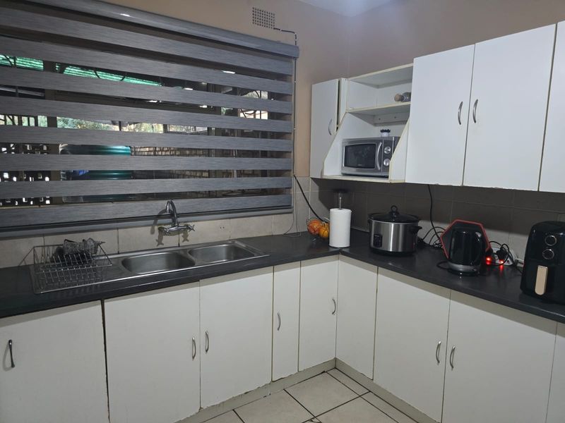 A functional kitchen featuring white cabinetry, dark laminate countertops, a double basin sink, and tiled flooring, providing a practical workspace for daily use.