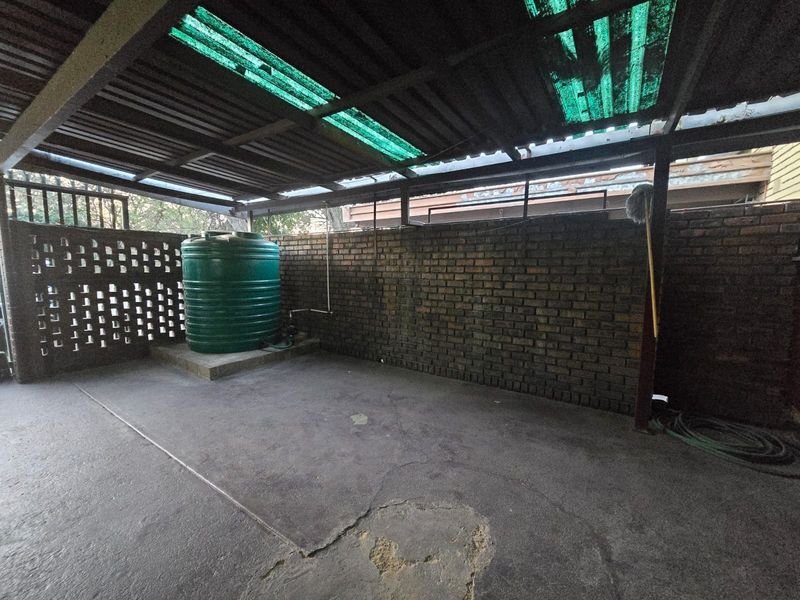 A covered utility area featuring a brick wall, concrete flooring, and a water storage tank under a corrugated roof structure.