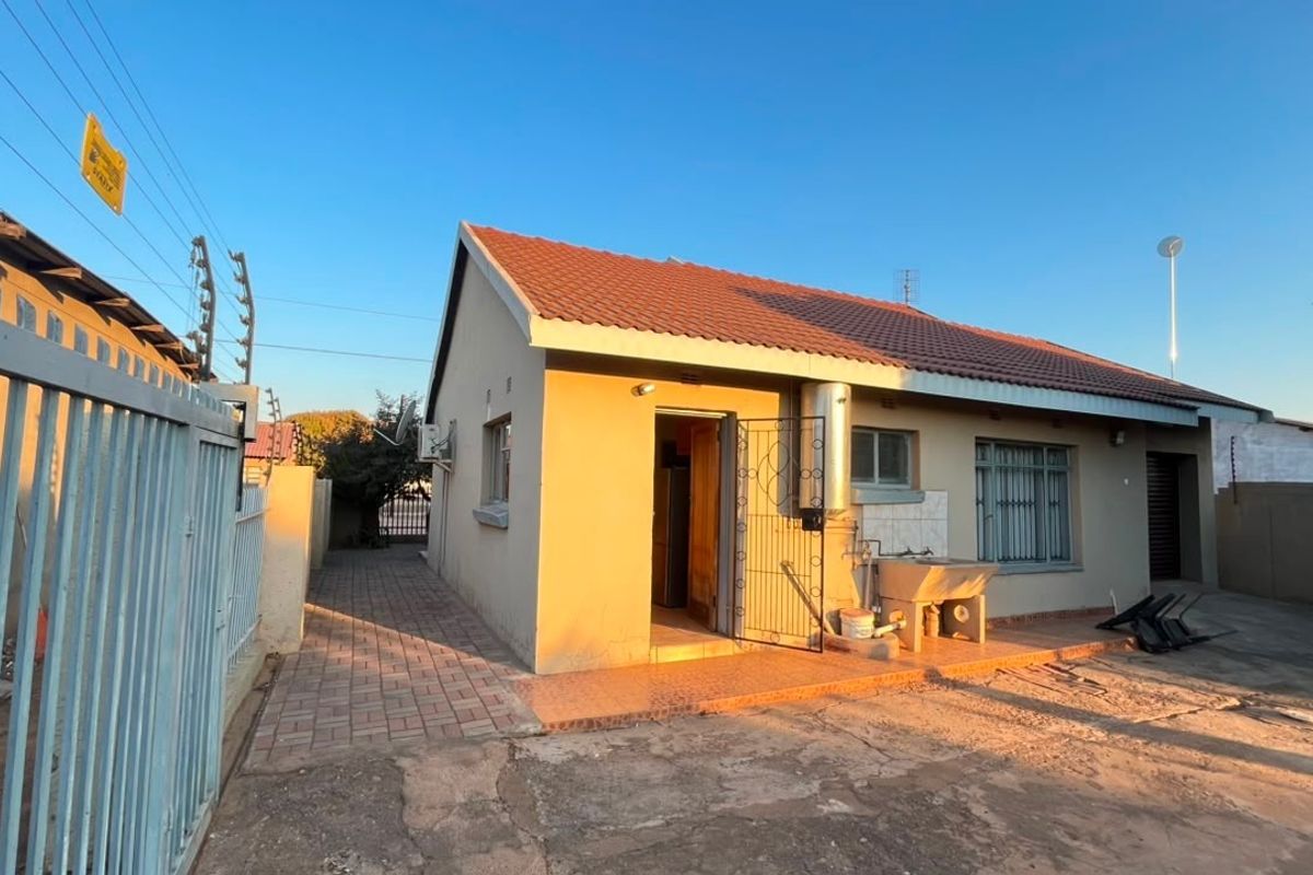 Rear exterior view of the house featuring a paved walkway, security gate, external laundry sink, and perimeter electric fencing.