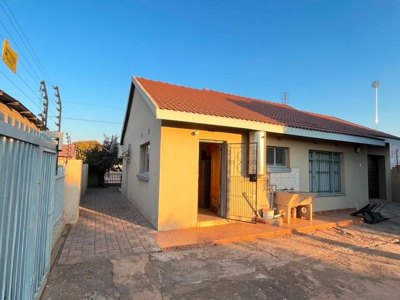 Rear exterior view of the house featuring a paved walkway, security gate, external laundry sink, and perimeter electric fencing.