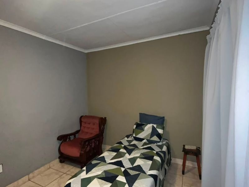 A simple bedroom featuring tiled flooring and neutral painted walls, providing a functional space for rest.