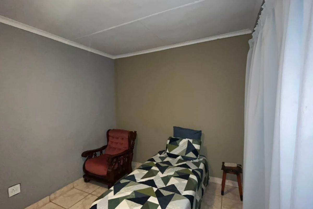 A simple bedroom featuring tiled flooring and neutral painted walls, providing a functional space for rest.