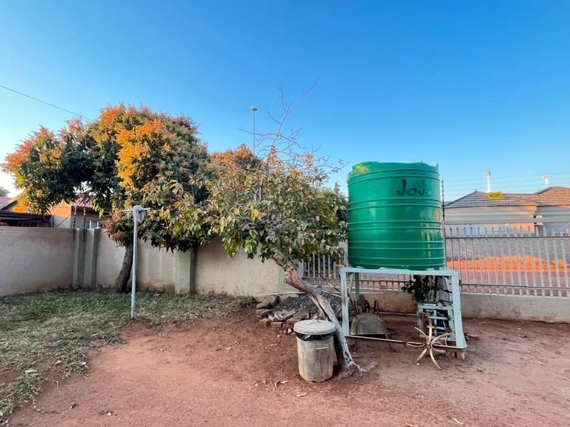 A backyard area featuring a water storage tank on a metal stand, enclosed by a perimeter wall and metal fencing.