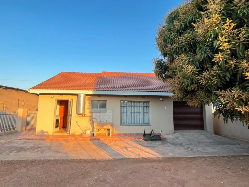 Front view of a single-story house featuring a tiled roof, concrete driveway, integrated garage, and external wash basin area.