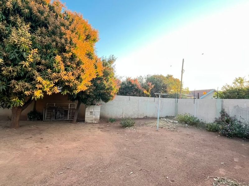 A spacious rear garden area featuring a perimeter wall with electric fencing, a rotary clothesline, and established trees.