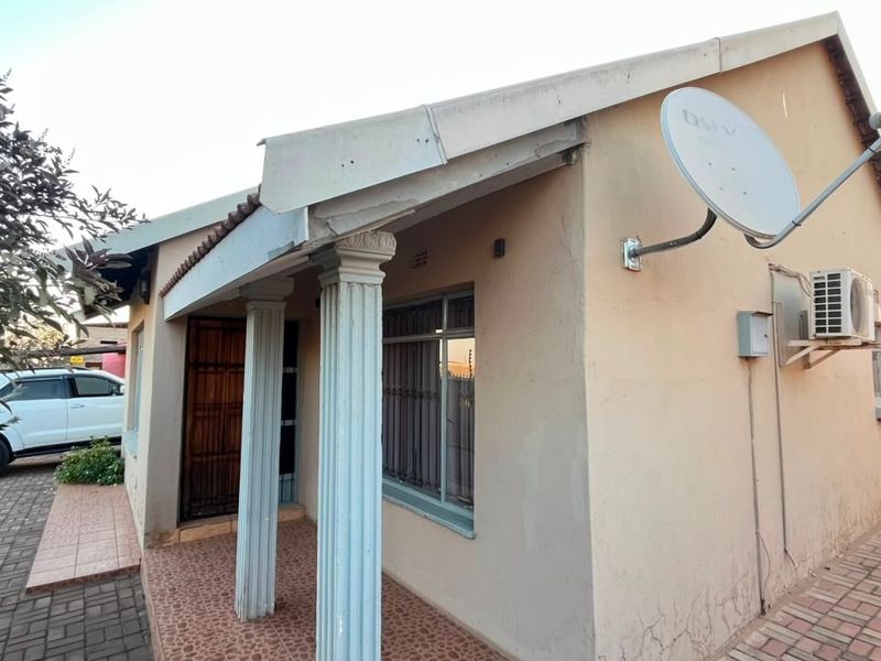 Front exterior view of a single-story house featuring a tiled porch with decorative columns, paved driveway, and mounted satellite dish.