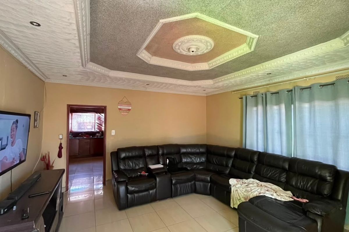 Spacious living room featuring tiled flooring, a decorative recessed ceiling with downlights, and a central ceiling rose.