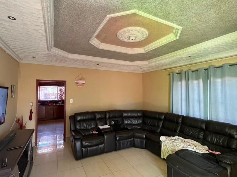 Spacious living room featuring tiled flooring, a decorative recessed ceiling with downlights, and a central ceiling rose.