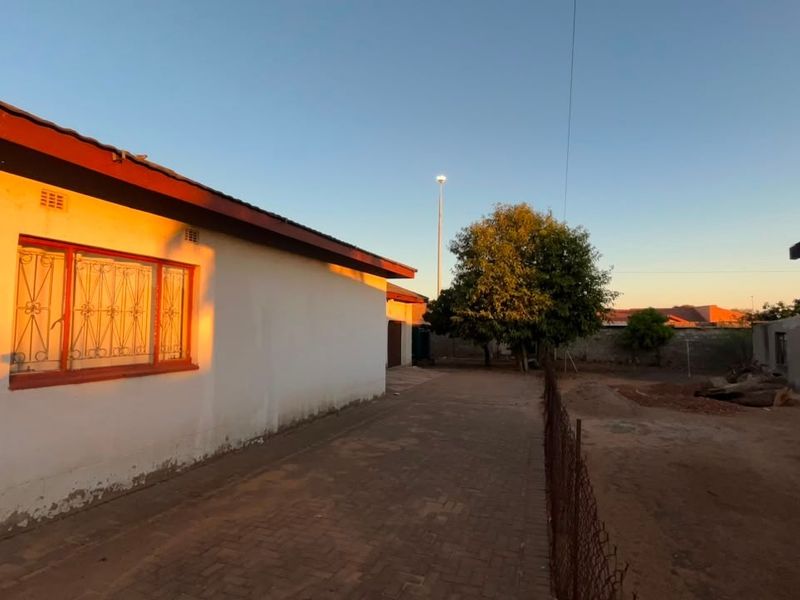 Rear exterior view of the property featuring a paved driveway, security bars on windows, and a perimeter wall with an unpaved yard area.