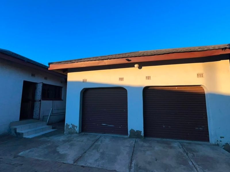 Exterior view of a double garage with roller doors and an adjacent entrance, featuring a concrete driveway and visible exterior wall maintenance requirements.
