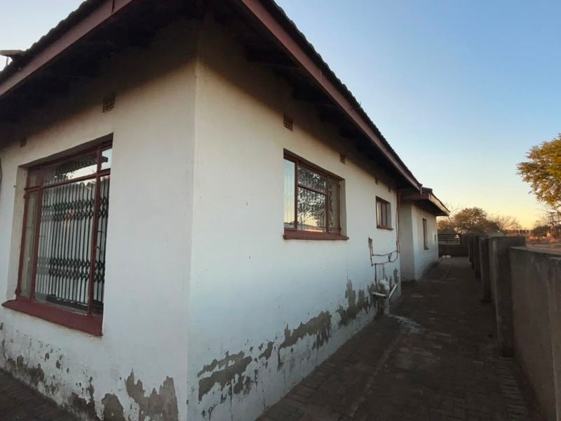 Rear exterior view of the house showing a paved walkway, boundary wall, and visible signs of exterior wall paint deterioration and damp.