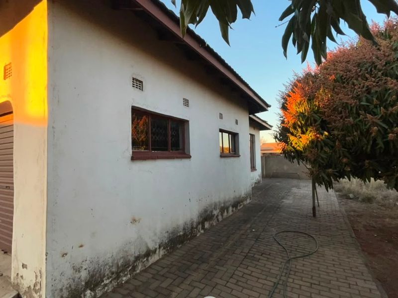 Rear exterior view of the property featuring a paved driveway, roller shutter garage door, and visible signs of exterior wall maintenance required.