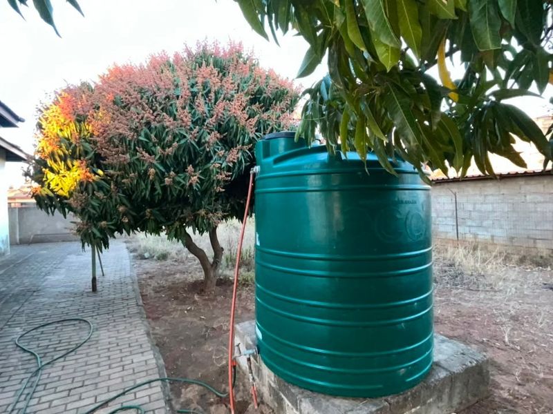 Rear exterior area featuring a green water storage tank mounted on a concrete plinth, adjacent to a paved walkway and masonry boundary wall.