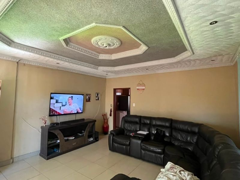 A living room featuring a decorative recessed ceiling with a central ceiling rose, downlights, and tiled flooring.