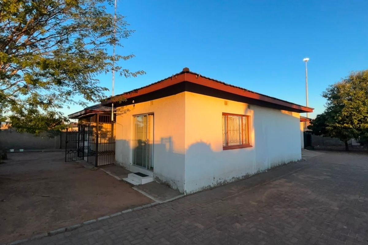 Rear view of a detached house featuring a tiled roof, security bars on windows, and a paved yard area.