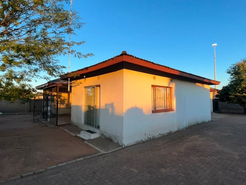 Rear view of a detached house featuring a tiled roof, security bars on windows, and a paved yard area.