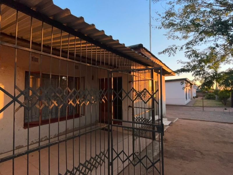 Rear exterior view of the property featuring a covered patio area with security gates and a paved driveway.
