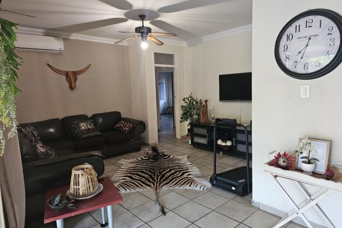A living room featuring tiled flooring, a ceiling fan, and a wall-mounted air conditioning unit.