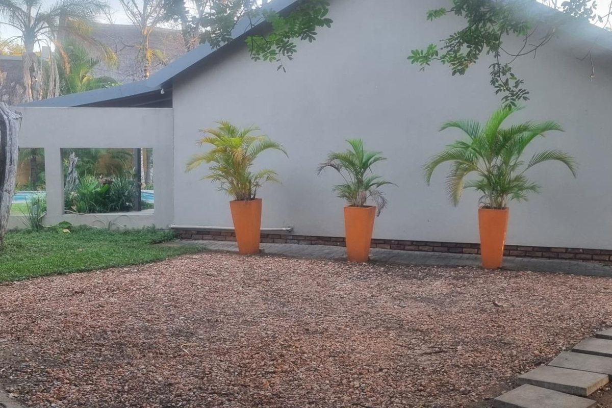 A rear exterior view featuring a gravel courtyard, paved pathways, and a boundary wall with decorative window cutouts.