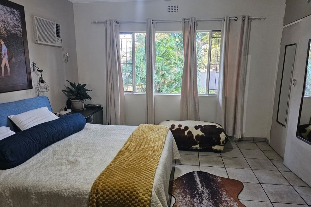 A bedroom featuring tiled flooring, a built-in wardrobe, and a window-mounted air conditioning unit, offering a functional and comfortable living space.