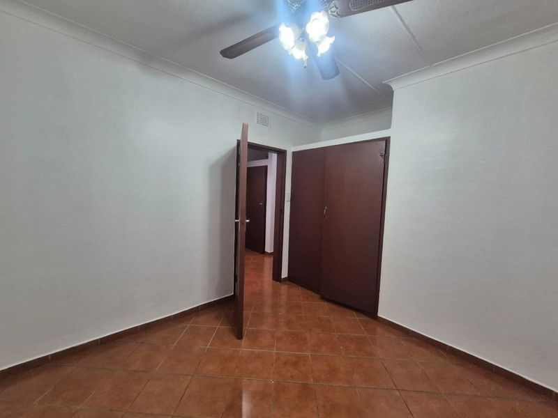 An empty bedroom featuring tiled flooring, a ceiling fan, and built-in cupboards, offering a blank canvas for personalization.