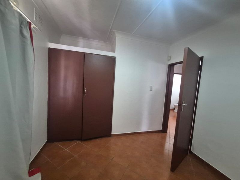 A simple bedroom featuring tiled flooring, a built-in wardrobe, and a coved ceiling, with an adjacent doorway leading to a bathroom.