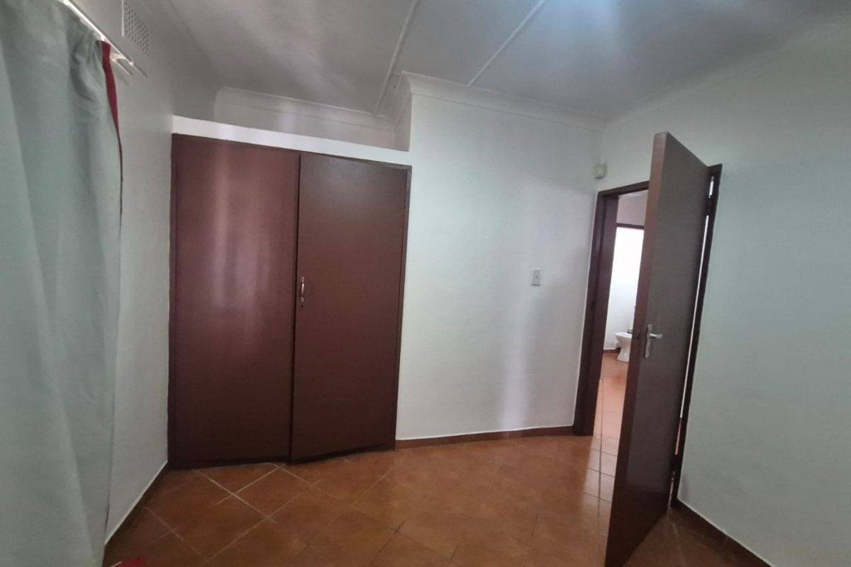 A simple bedroom featuring tiled flooring, a built-in wardrobe, and a coved ceiling, with an adjacent doorway leading to a bathroom.