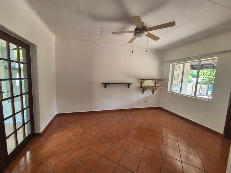 A bright, empty living room featuring terracotta floor tiles, a ceiling fan, and direct access to the exterior through a classic french door.