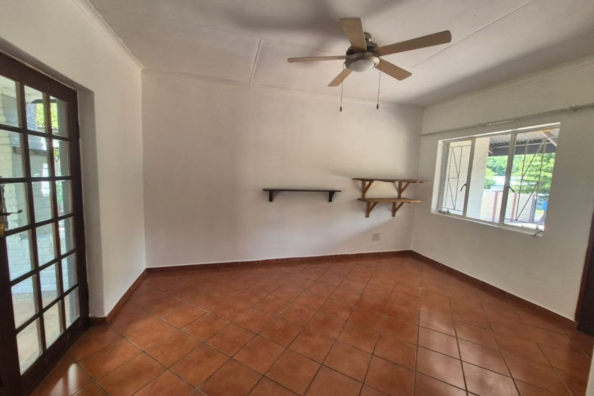 A bright, empty living room featuring terracotta floor tiles, a ceiling fan, and direct access to the exterior through a classic french door.