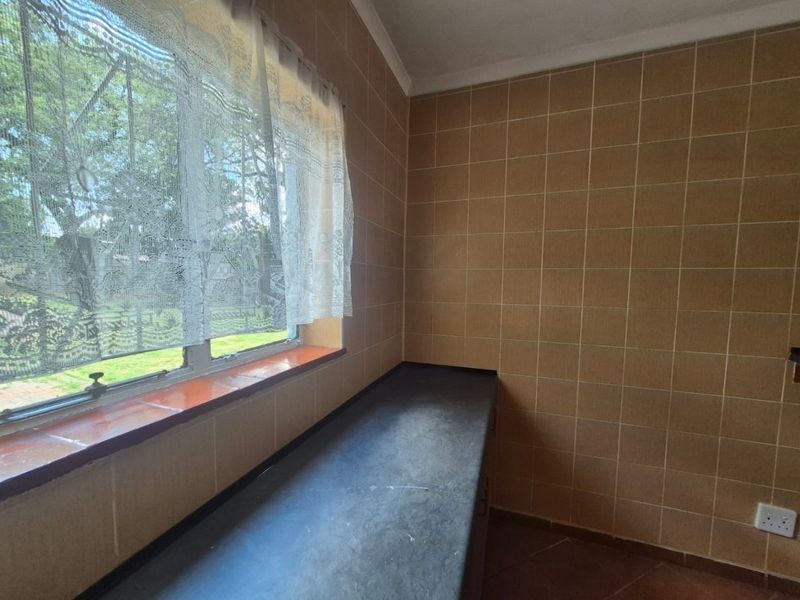 A functional scullery or utility area featuring tiled walls, a dark laminate countertop, and a window overlooking the garden.
