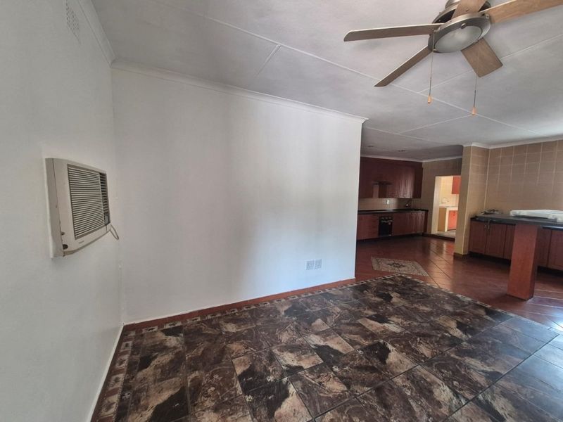 Spacious open-plan living and kitchen area featuring tiled flooring, a ceiling fan, wall-mounted air conditioning, and functional built-in cabinetry.