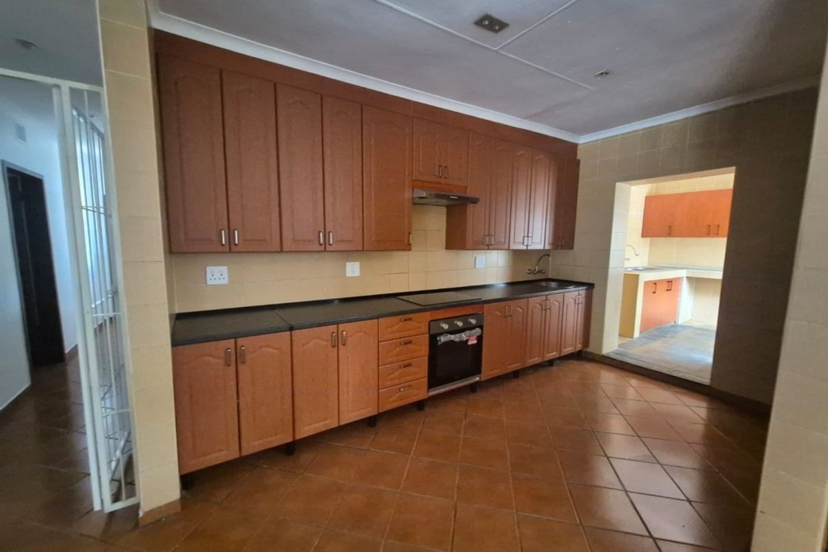 A functional kitchen featuring wooden cabinetry, built-in oven, extractor fan, and tiled flooring, with an adjacent scullery area.